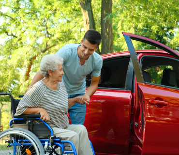 A man assisting an elderly woman into a car, showing kindness and support.