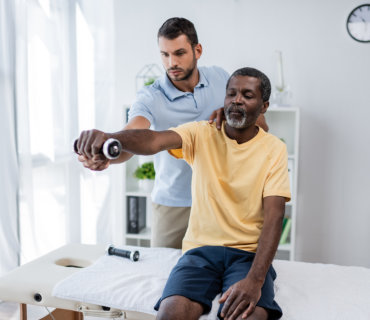 a health professional assists a senior man doing arm exercise