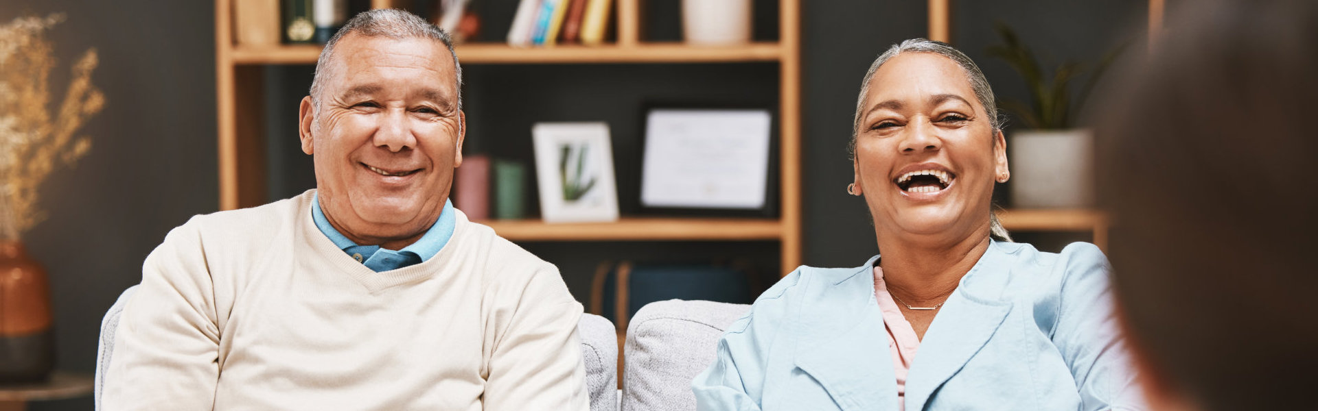 Two elderly individuals happily seated on a sofa.